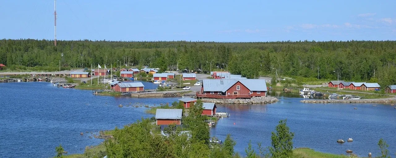 Pieni suomalainen kalastajakylä: punaisia taloja, veneitä ja metsää veden äärellä. Pieni suomalainen kalastajakylä: punaisia taloja, veneitä ja metsää veden äärellä.